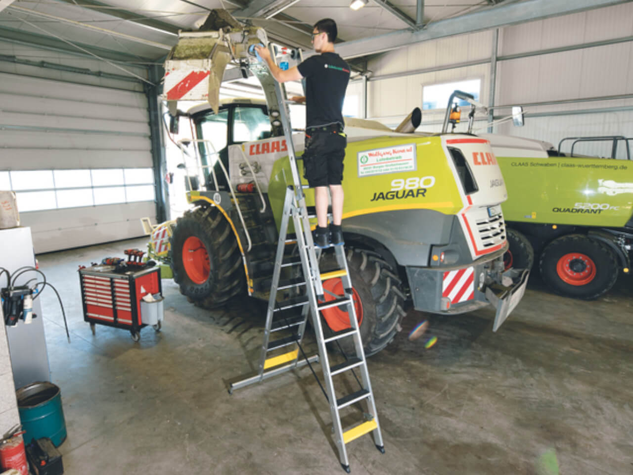 mechaniker in der landwirtschaft arbeitet an einer maschine auf einer munk mehrzweckleiter